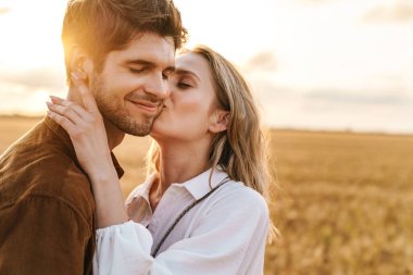 Kırsalda altın tarlada öpüşen ve kucaklaşan beyaz güzel bir çiftin görüntüsü.
