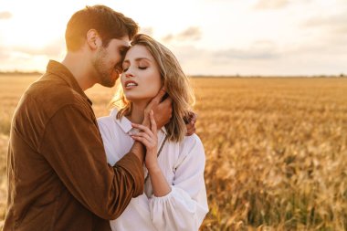 Kırsalda altın tarlada sarılan beyaz güzel bir çiftin görüntüsü.