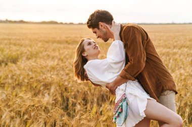 Kırsalda altın tarlada sarılan beyaz güzel bir çiftin görüntüsü.