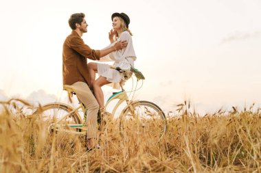 Kırsalda birlikte bisiklete binen ve gülümseyen beyaz bir çift.