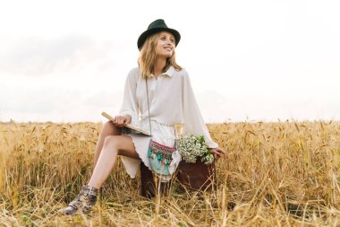 Kırsal kesimde altın tarlada otururken kitap okuyan genç sarışın beyaz kadın.