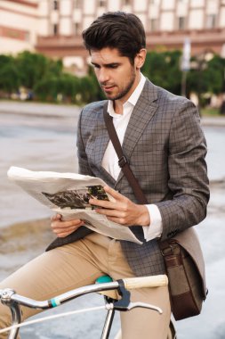 Dışarıda bisikletle gazete tutan yakışıklı, konsantre bir iş adamının görüntüsü.