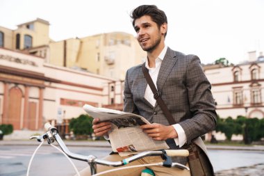 Dışarıda bisikletle gazete tutan iyimser bir iş adamının resmi.