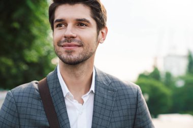 Dışarıda çantalı, iyimser, yakışıklı bir iş adamının resmi.