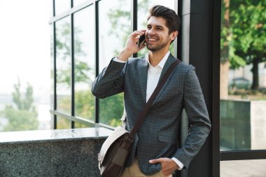 İyimser, neşeli, yakışıklı iş adamının dışarıda cep telefonuyla iş merkezinin yakınında konuşması.