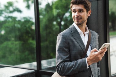 Dışarıda cep telefonu kullanan iyimser ve yakışıklı bir iş adamının resmi