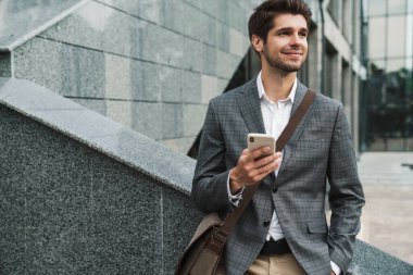 İş merkezinin yakınında cep telefonu kullanan mutlu ve yakışıklı bir iş adamı resmi.