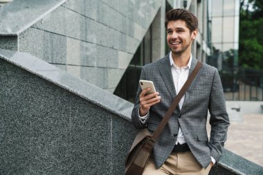 İş merkezinin yakınında cep telefonu kullanan, mutlu ve yakışıklı bir iş adamı görüntüsü