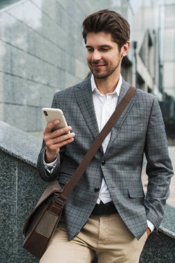 İş merkezinin yakınında cep telefonu kullanan mutlu ve yakışıklı bir iş adamı resmi.