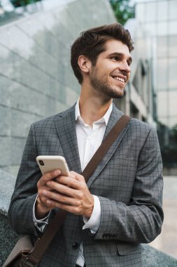 Şehir caddesinde gülümseyen ve cep telefonu kullanan ceketli mutlu bir iş adamı resmi