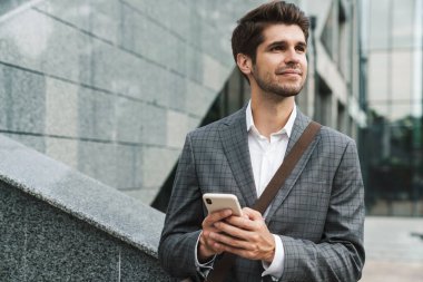 Şehir caddesinde gülümseyen ve cep telefonu kullanan ceketli mutlu bir iş adamı resmi