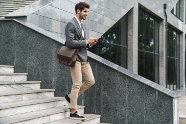 Merdivenlerden inerken cep telefonu kullanan neşeli, yakışıklı bir iş adamı.