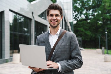 İş merkezinin yakınındaki dizüstü bilgisayarı kullanan iyimser ve yakışıklı iş adamının resmi