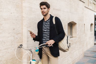 Şehir caddesinde cep telefonu kullanan bisikletli yakışıklı bir adamın görüntüsü.