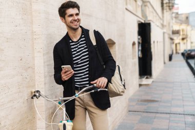 Ceketli, bisikletli, gülümseyen ve cep telefonu kullanan yakışıklı bir adam.
