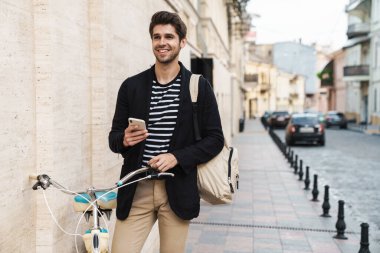 Dışarıda bisikletle akıllı telefon kullanan mutlu bir iş adamının resmi.