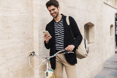 Dışarıda bisikletle akıllı telefon kullanan neşeli bir iş adamının resmi.