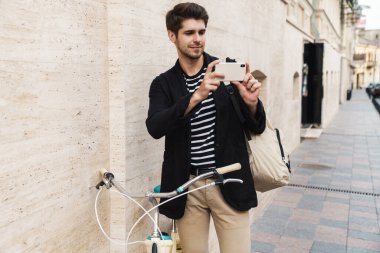 Dışarıda bisikletli bir akıllı telefonla fotoğraf çeken genç ve memnun bir iş adamının resmi.