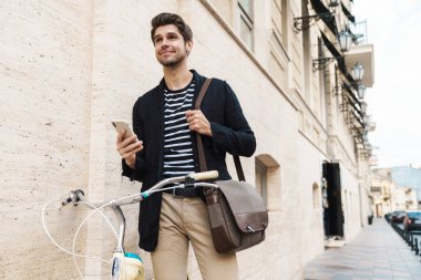 Dışarıda bisikletle akıllı telefon kullanan mutlu bir iş adamının resmi.