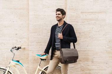 Dışarıda bisikletle gezen, gülümseyen genç ve yakışıklı bir iş adamının fotoğrafı.