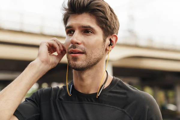 在城市街道上工作时使用耳机的体育高加索运动员形象 — 图库照片