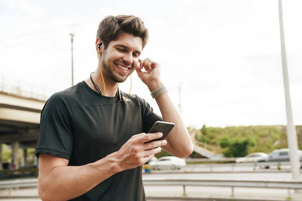 Εικόνα Του Χαμογελαστού Νεαρού Αθλητή Ακουστικά Χρησιμοποιώντας Κινητό Τηλέφωνο Ενώ — Φωτογραφία Αρχείου