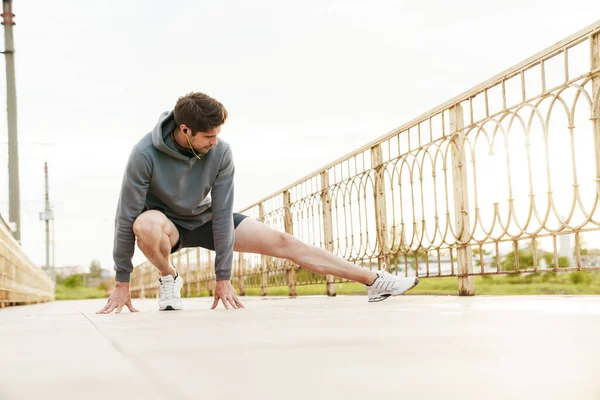 街の橋で働きながら運動をするイヤホンの若い白人スポーツマンのイメージ — ストック写真