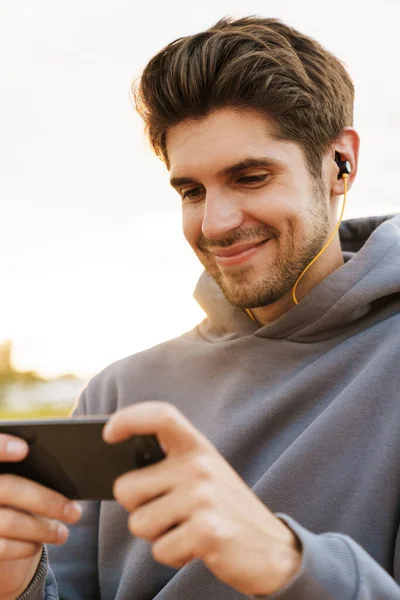 Bild Leende Man Med Hörlurar Spela Dataspel Mobiltelefon Utomhus — Stockfoto