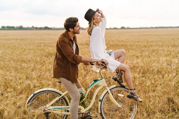 田舎で一緒に笑顔で自転車に乗る若い白人夫婦のイメージ — ストック写真