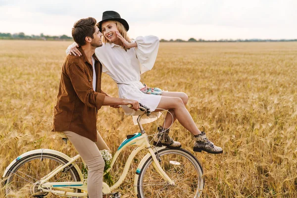 Kırsalda birlikte bisiklete binen ve gülümseyen beyaz bir çift.
