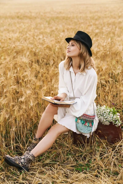 田舎の黄金のフィールドに座っている間若いブロンドの白人女性の読書本のイメージ — ストック写真