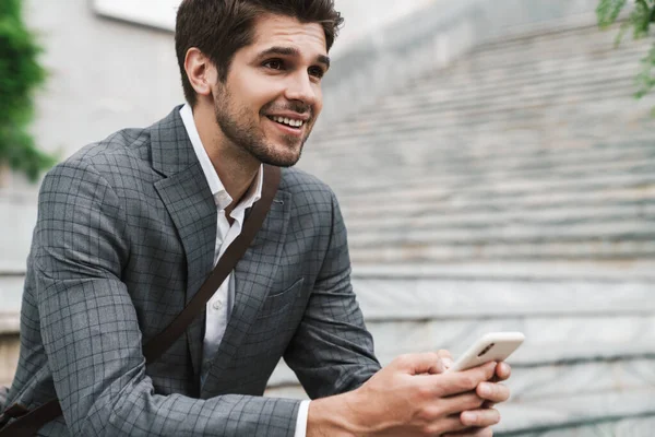 Kép Mosolygó Pozitív Jóképű Üzletember Szabadban Mobiltelefonnal Miközben Lépcsőn — Stock Fotó