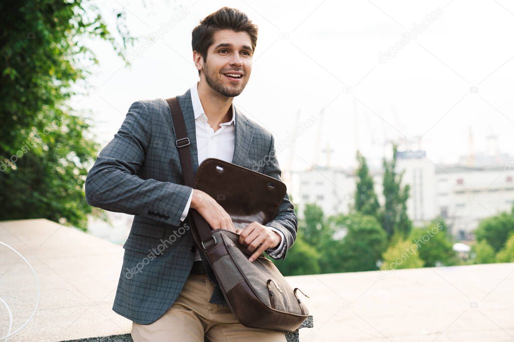 Image of a cheery smiling handsome business man outdoors with bag