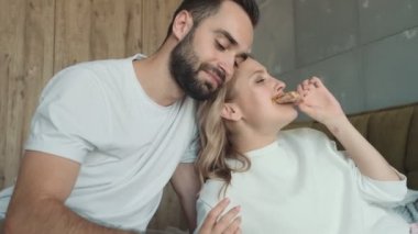 Olumlu bir çift, evdeki yatakta otururken birlikte pizza yiyor.