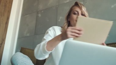 Pozitif bir genç kadın, evdeki yatağında otururken dizüstü bilgisayarındaki video bağlantısını kullanarak birine kağıt belgeler gösteriyor.