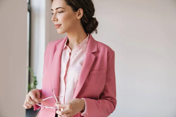 Foto Hermosa Mujer Complacida Chaqueta Rosa Sosteniendo Las Gafas Mientras —  Fotos de Stock