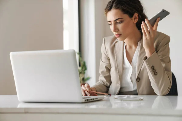 Photo Confident Focused Woman Using Mobile Phone While Working Laptop — Stock Photo, Image