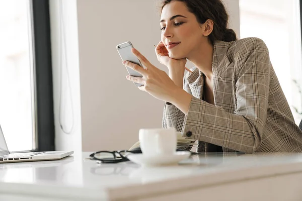 Photo Pleased Nice Woman Smiling Using Mobile Phone While Working — Stock Photo, Image