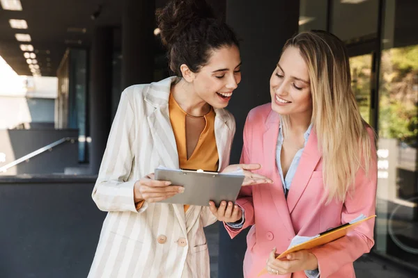 İki güzel gülümseyen genç iş kadını şehir sokaklarında yürüyorlar, ellerinde klasörlerle bir projeyi tartışıyorlar.