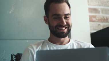 Yakışıklı genç bir adam laptopunu içeride otururken kullanıyor.