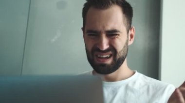 Kızgın bir genç adam bilgisayarını evde otururken kullanıyor.