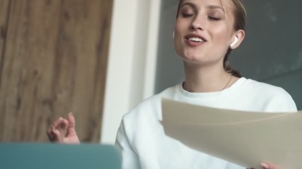 Удовлетворенная Молодая Женщина Наушниками Разговаривает Кем Используя Ноутбук Показывая Бумажные — стоковое видео