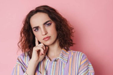 Kızıl saçlı, poz veren ve pembe arka planda izole edilmiş kameraya bakan ciddi bir kadın resmi.