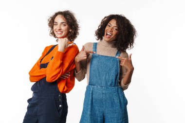 Tulum giymiş iki neşeli kadının portresi gülümseyen ve beyaz arka planda izole edilmiş parmakları gösteren.