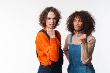 Tulumlu kızgın çok uluslu kadınların portresi beyaz arka planda izole edilmiş kameraya yumruklarını gösteriyor.