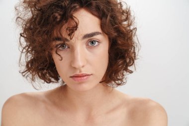 Beyaz arka planda izole edilmiş kısa kıvırcık kahverengi saçlı çekici, üstsüz bir kadının güzel portresi. Kameraya bakıyor.