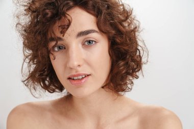 Beyaz arka planda izole edilmiş kısa kıvırcık kahverengi saçlı çekici, üstsüz bir kadının güzel portresi. Kameraya bakıyor.