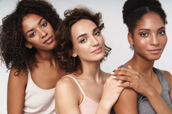 Beyaz arka planda birbirine sarılan üç sevimli kadının portresi.