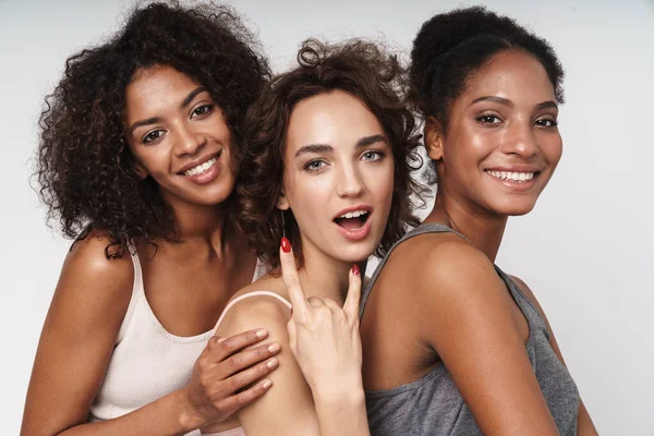 Üç mutlu çoklu etnik kadının portresi gülümseyen ve boynuz parmaklarını beyaz arka planda izole bir şekilde gösteren