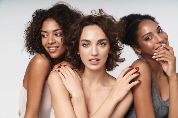 Çok ırklı üç kadının portresi. Beyaz arka planda izole edilmiş kameraya sarılıp gülümsüyorlar.